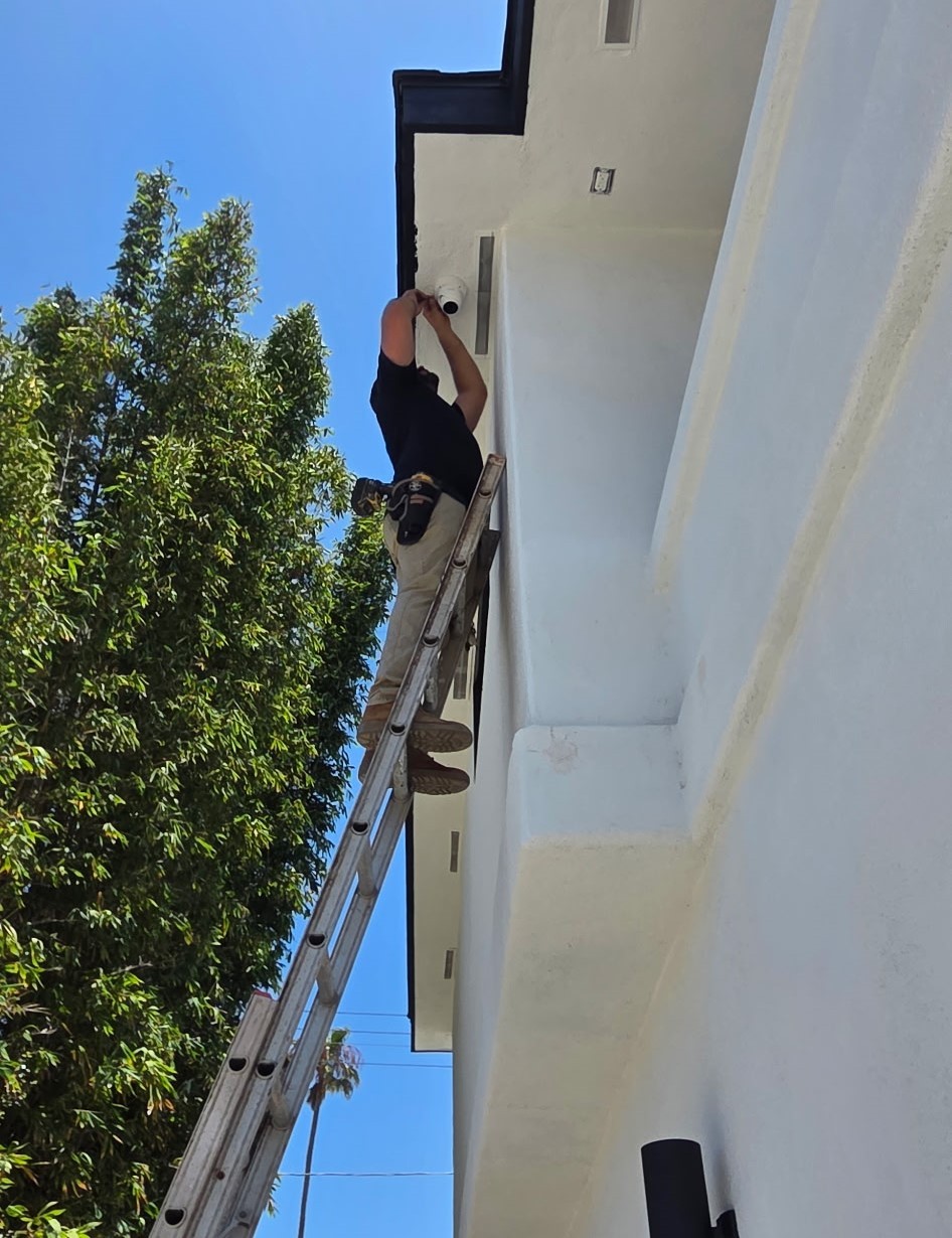 SSI technician on a ladder installing a new dome camera under the eave of a home