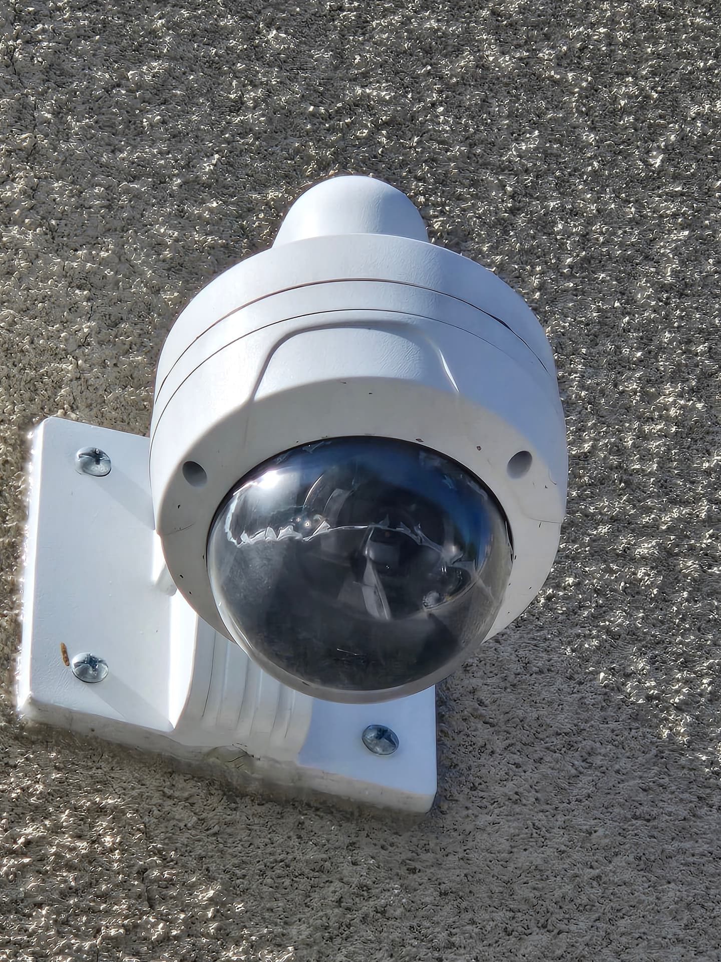 Wall-mounted white dome security camera on a stucco exterior with a clouded, weather-worn lens cover